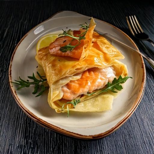 Golden, crispy fish wrapped in flaky filo pastry, garnished with fresh herbs and served with a side of lemon wedges.